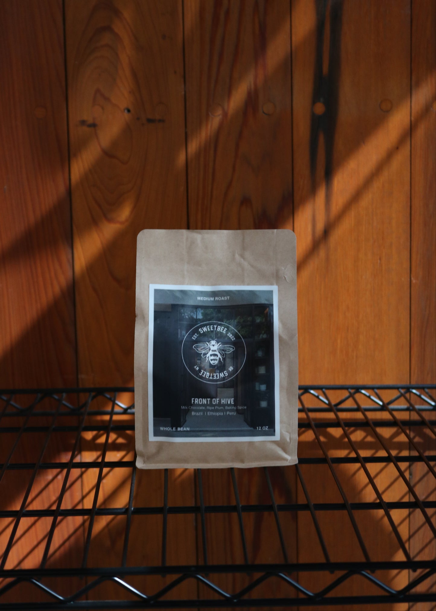 A sealed bag of coffee beans labeled 'Front of Hive' placed on a shelf with wood panel background.