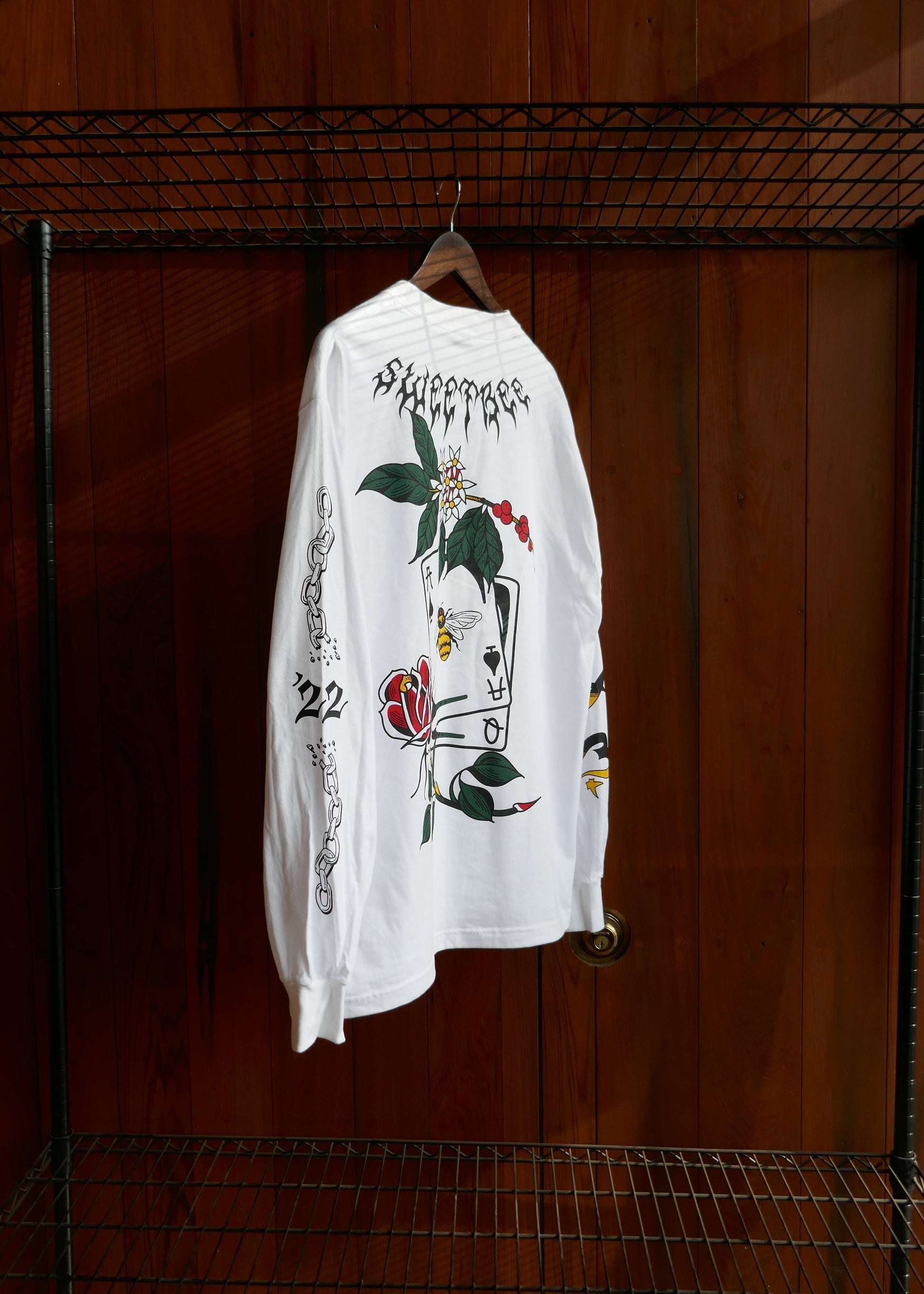 White t-shirt with black and red graphics in a wire dog crate against a wooden wall.