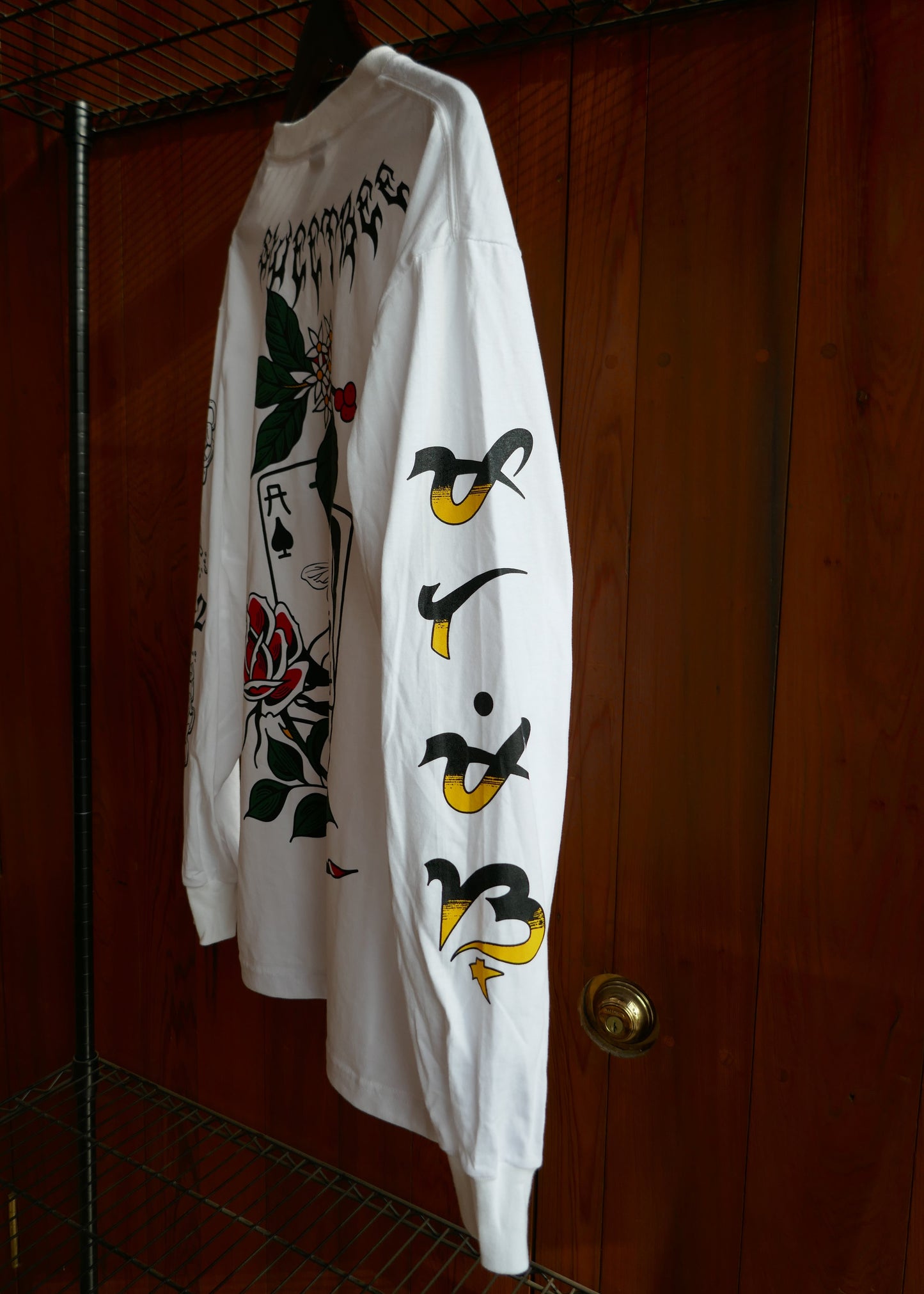 White t-shirt with black and yellow designs down the arm on a wooden surface