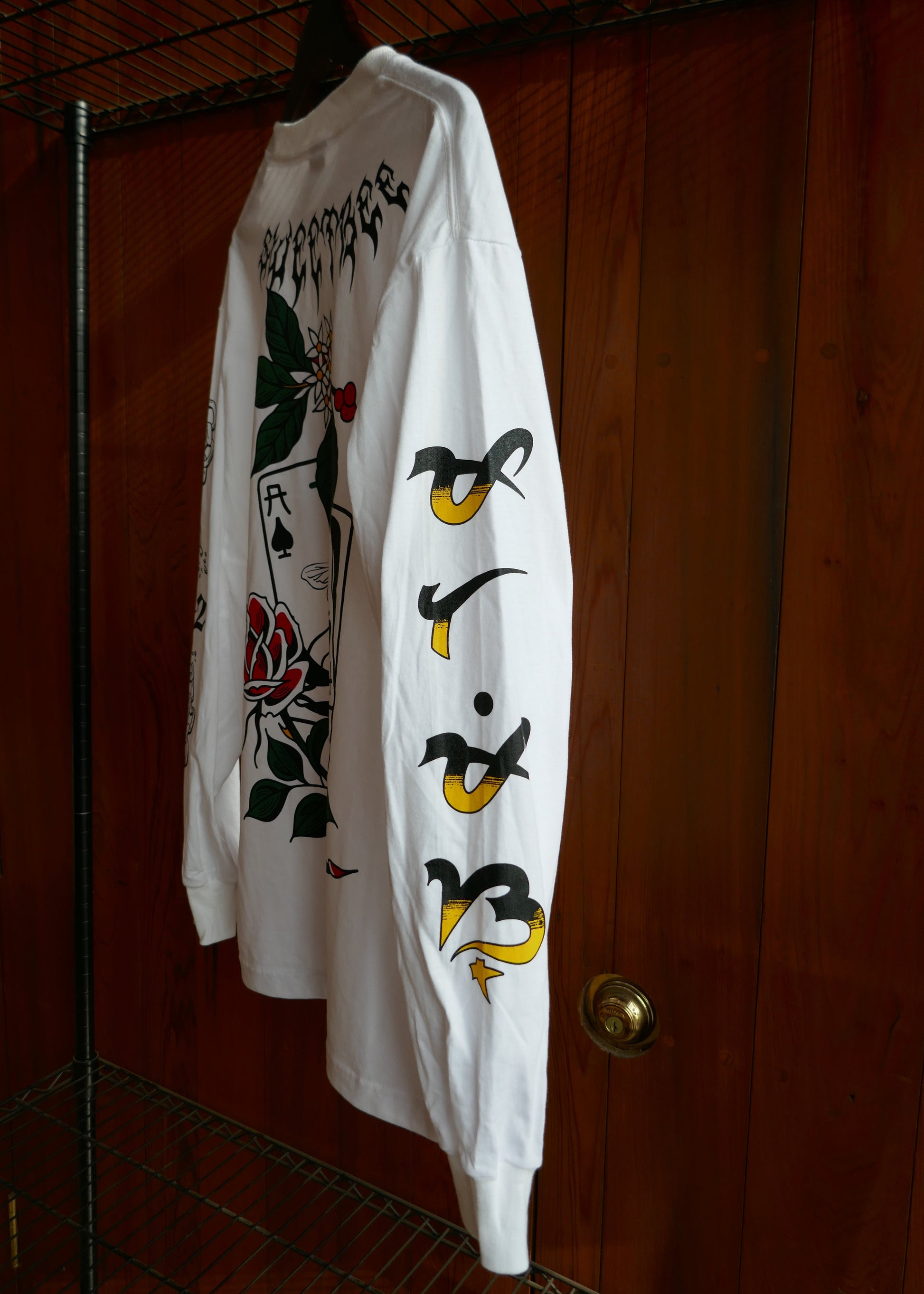 White t-shirt with black and yellow designs down the arm on a wooden surface