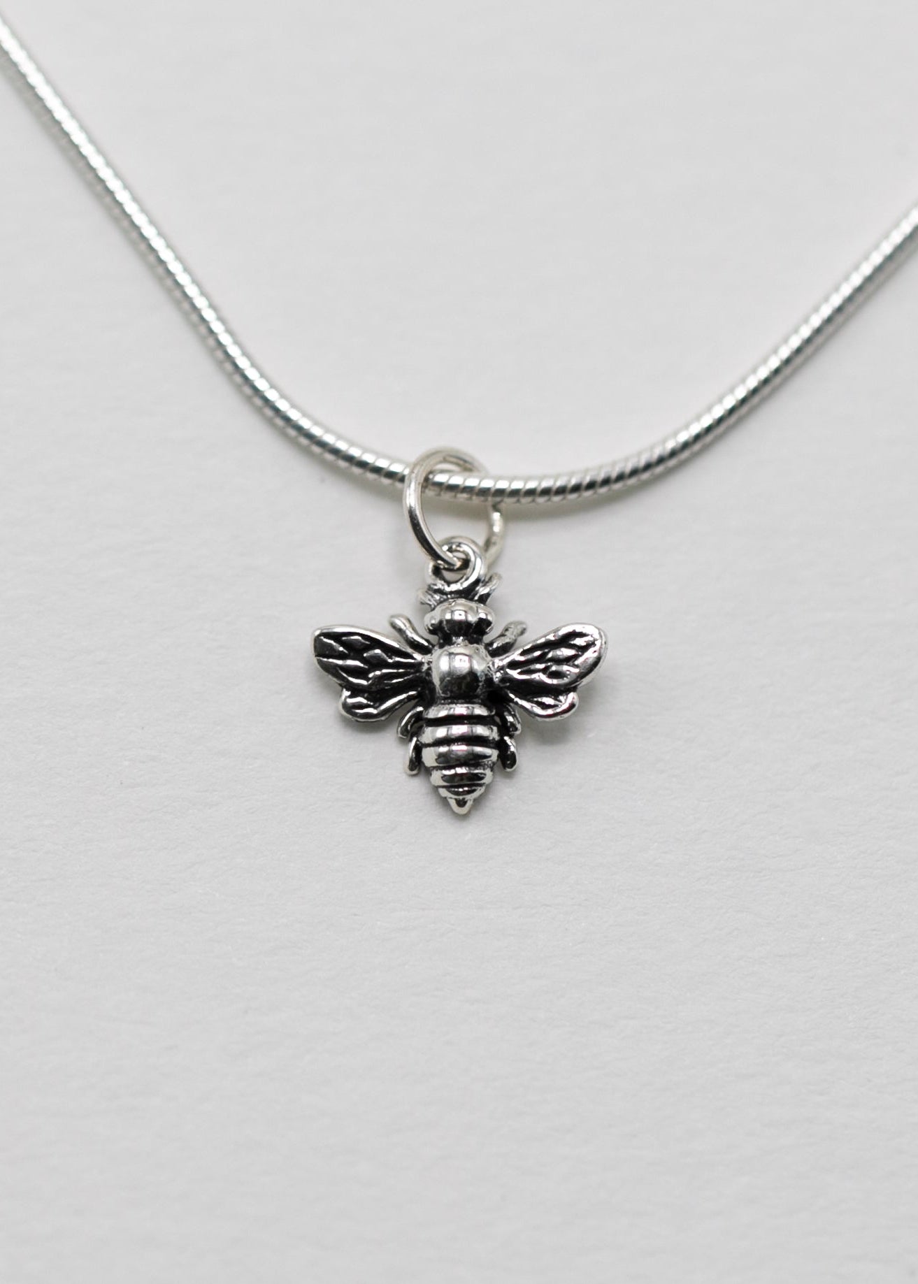 sterling Silver bee pendant on a sterling silver snake chain against a light gray background